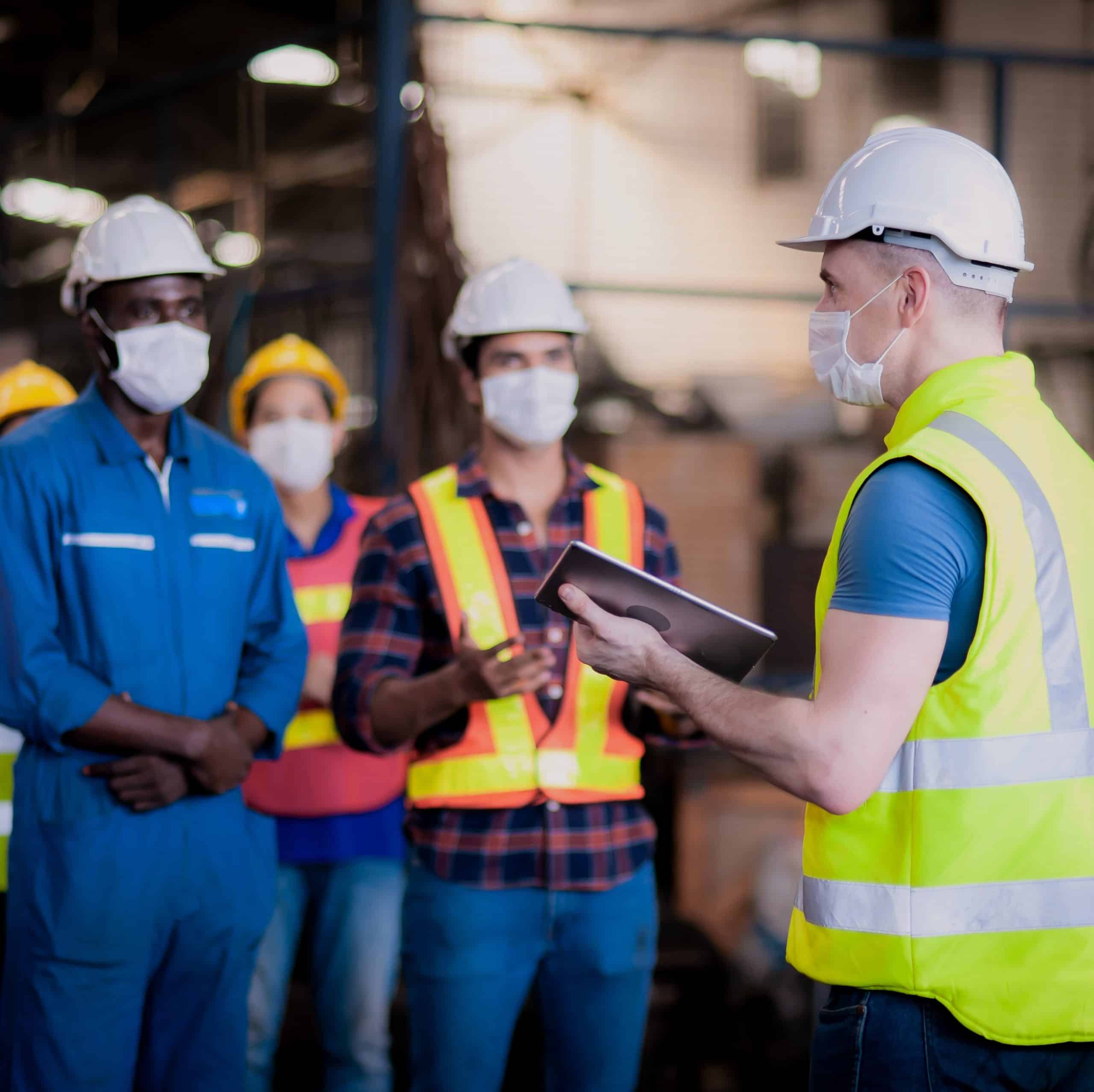 Safety meeting with construction workers wearing hard hats and masks at Gulf Coast construction site, emphasizing safety protocols and teamwork.