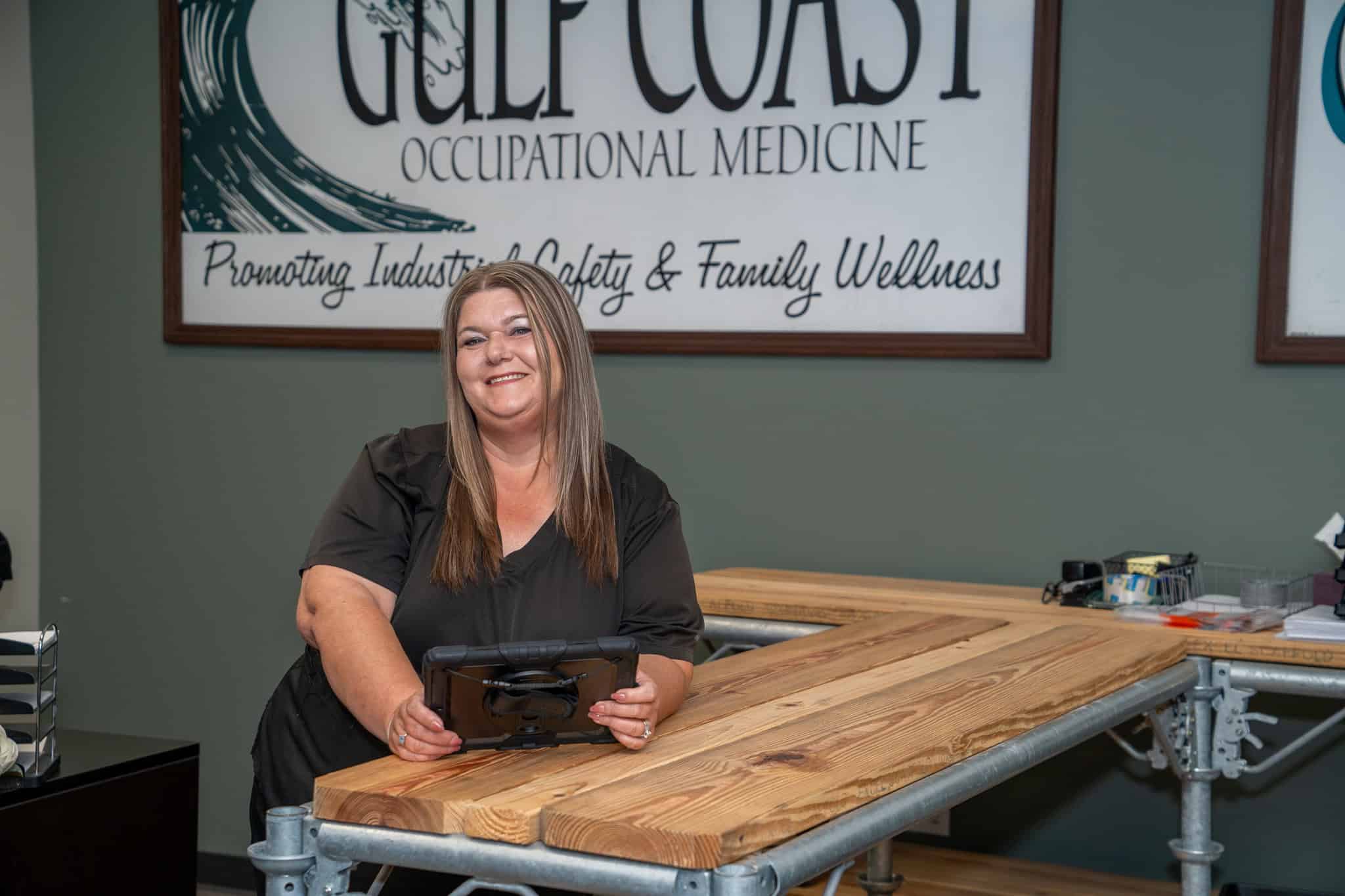 Gulf Coast occupational medicine clinic staff member smiling at reception desk promoting industry safety and family wellness.