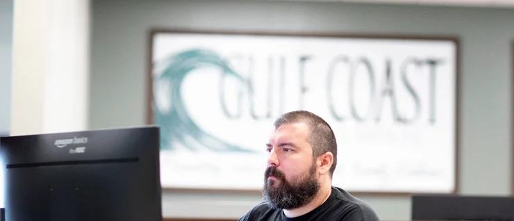 Gulf Coast office staff working at a reception desk with Gulf Coast branding in the background, emphasizing professional service and coastal community engagement.